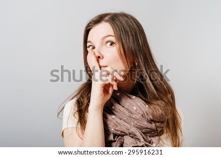 Young woman shows silence finger to his mouth. On a gray background.