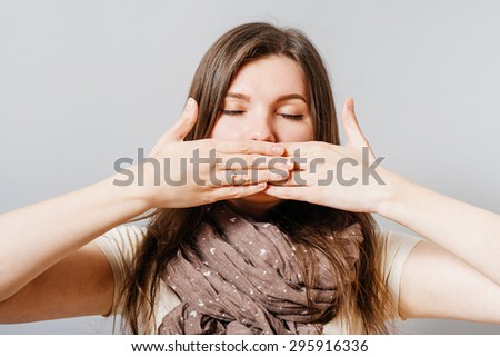 Young woman closed her eyes and covered her mouth with her hands. On a gray background.