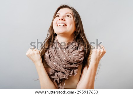 Young woman shows gesture of victory, joy, success. On a gray background.