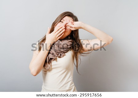 A young woman yawns. On a gray background.