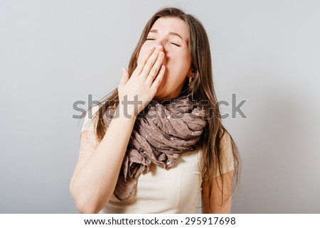 A young woman yawns. On a gray background.
