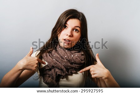 Young woman showing fingers on himself. On a gray background.