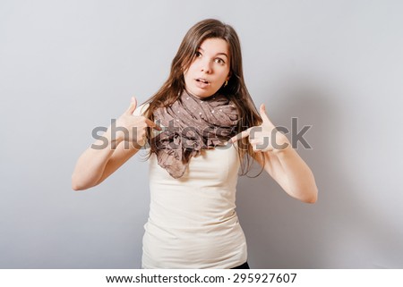 Young woman showing fingers on himself. On a gray background.