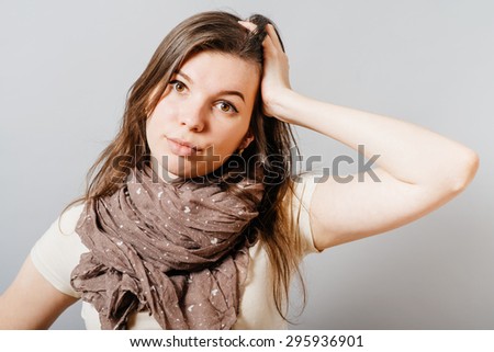 Young woman lost in thought, says, the hand behind the ear. On a gray background.