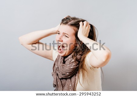 Young woman screams, tears her hair in anger. On a gray background.