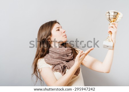 Young pretty woman with a golden cup victory. On a gray background.