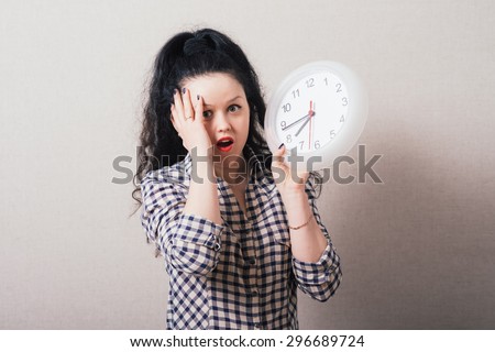 A woman looks at a wall clock with a hand on his head. On a gray background.
