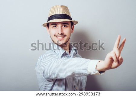 young casual man in hat showing victory sign while holding a hand in his pocket.
