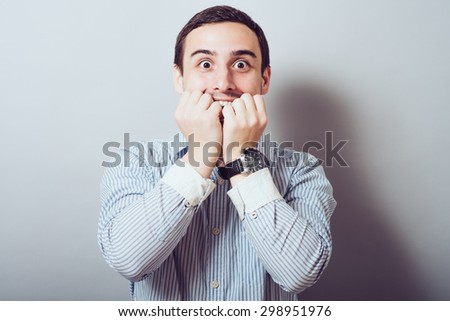 young business man biting his nails while looking into the camera. on a light gray studio background