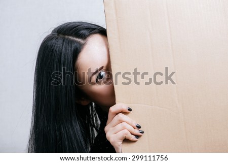 Woman peeping from behind empty cardboard. On a gray background.