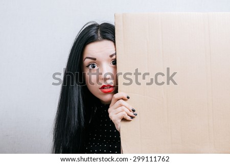 Woman peeping from behind empty cardboard. On a gray background.