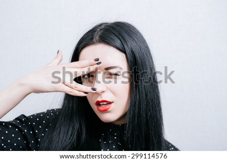 Woman afraid of look through your fingers. On a gray background.