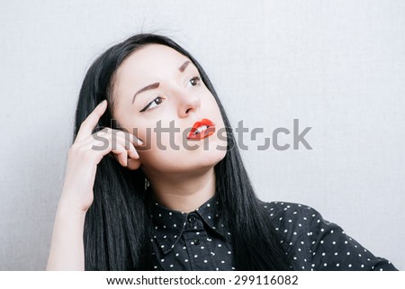 Elegant woman thinks finger to her temple. On a gray background.