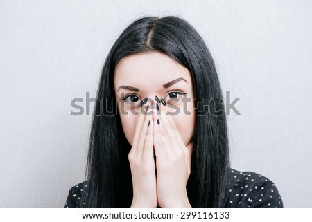 Woman surprised by covering her mouth with her hands. On a gray background.