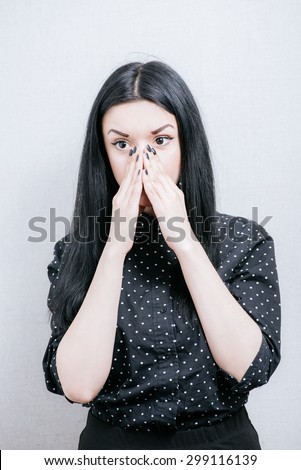Woman surprised by covering her mouth with her hands. On a gray background.