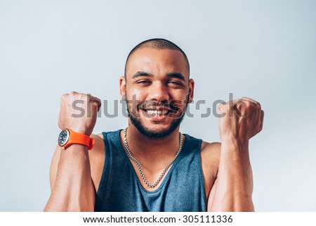A very happy and attractive african businessman wearing a corporate grey suit and blue tie punching the air with his fists arms in air, smiling and shouting in victorious success for his business deal
