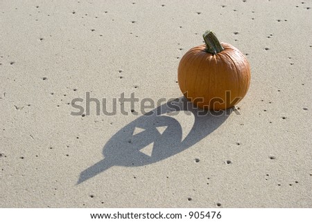 Pumpkin on the sand with face cut out of the shadow.