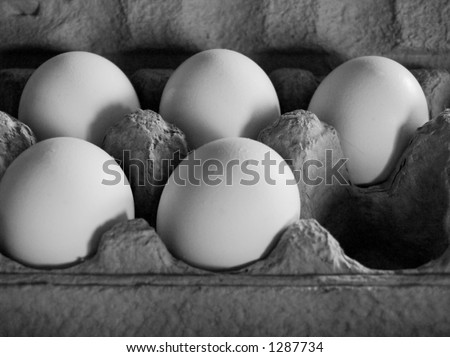 Five eggs in soft, dim light in a grey carton, arranged as to imply that an egg at the corner has been removed. Greyscale image.