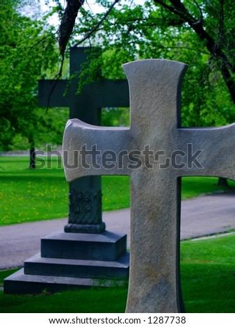 Two large crosses in a cemetery, admidst deep green foliage and moody lighting.