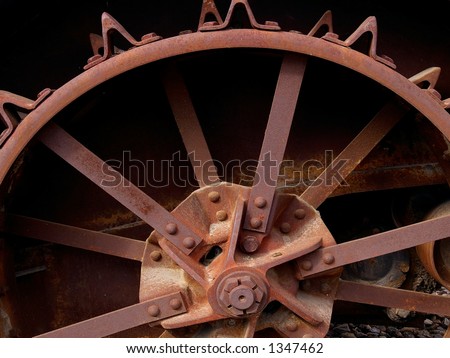 Old rusty steel wheel on ancient farming equipment showing triangle-shaped traction or tread devices.
