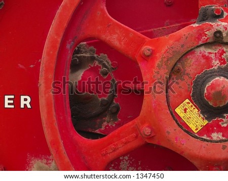 Steel crank wheel painted a bright red and covered in dirt on an old hay baling machine.