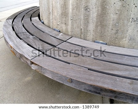 An urban plaza bench made of wood and concrete in strong light, shadow, and contrast.