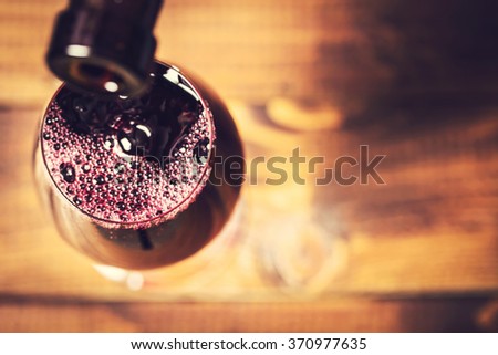 Pouring red wine into the glass against wooden background. Soft focus