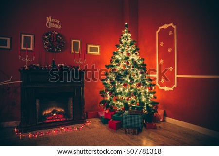 Beautiful new year room with decorated Christmas tree, gifts and fireplace with the glowing lights at night. The idea for postcards. Soft focus. Shallow DOF