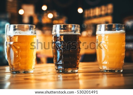 Beautiful background of the Oktoberfest. Glasses of cold fresh white, light and dark beer on the wooden bar counter in the pub. Assorted alcohol in a Flight Ready for Tasting.