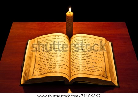 A bible open on a table next to a candle