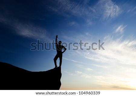 silhouette of a businessman with a laptop in hand is on top of a mountain in the sky with clouds.