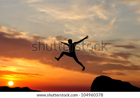 silhouette of a man jumping off a cliff in the direction of the bright sun