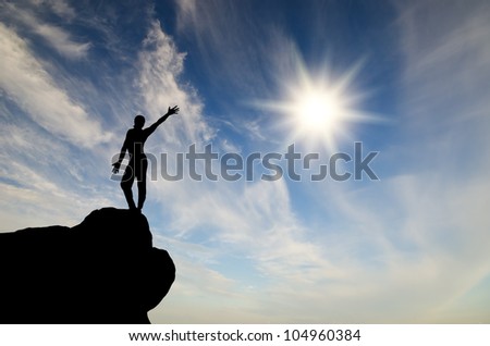 silhouette of a businessman with a laptop in hand is on top of a mountain in the sky with clouds.