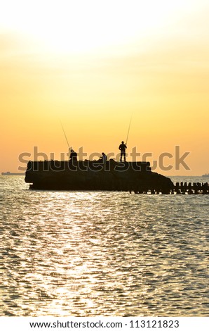 fishermen catch fish on a rock in the sea at sunset
