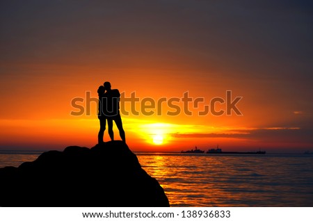 silhouettes man and woman standing on the hills Sea coast on the background of sunset