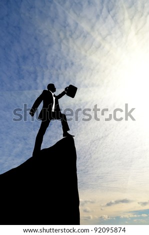 silhouette of a businessman with briefcase in hand up the mountain on the background of the cloudy sky