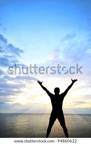 silhouette of a man on the beach with their hands up against the sunny sky