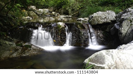 Swift moving water rushes past large boulders and over a small waterfall.