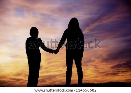 A mother and daughter holding hands watch the sunset.