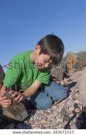 A young boy looks under a rock to see what is under there.