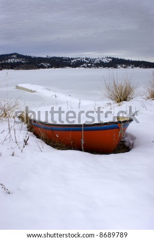 A snow filled boat by a frozen lake.