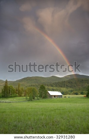 A rainbow in a dark cloudy sky rises above this barn.
