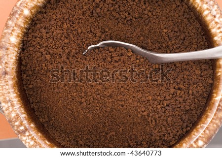 A spoon is partly buried in dry coffee grounds.