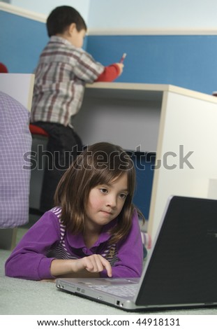 A young girl uses the laptop while her younger brother draws at the desk.