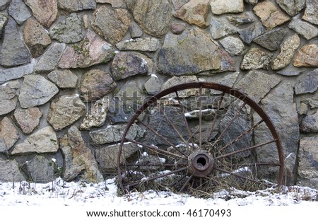 An old wagon wheel is displayed against a rock wall.