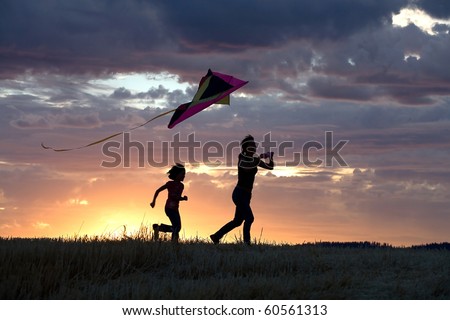 A mother runs to fly a kite with her daughter behind her.