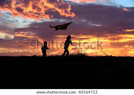 A girl flies a kite at sunset while her brother runs after.