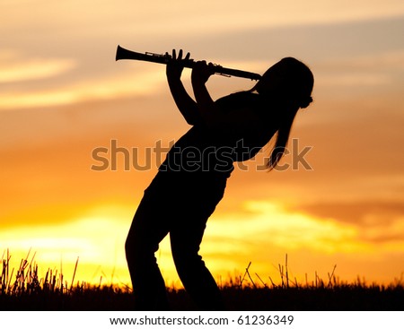 A silhouetted woman plays the Clarinet at sunset.