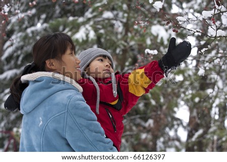 A boy being held by his mother reaches up for snow covered berries.