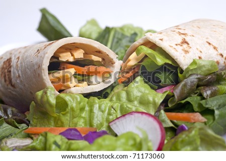 A veggie wrap with fresh veggies and veggie cheese on top of a salad.